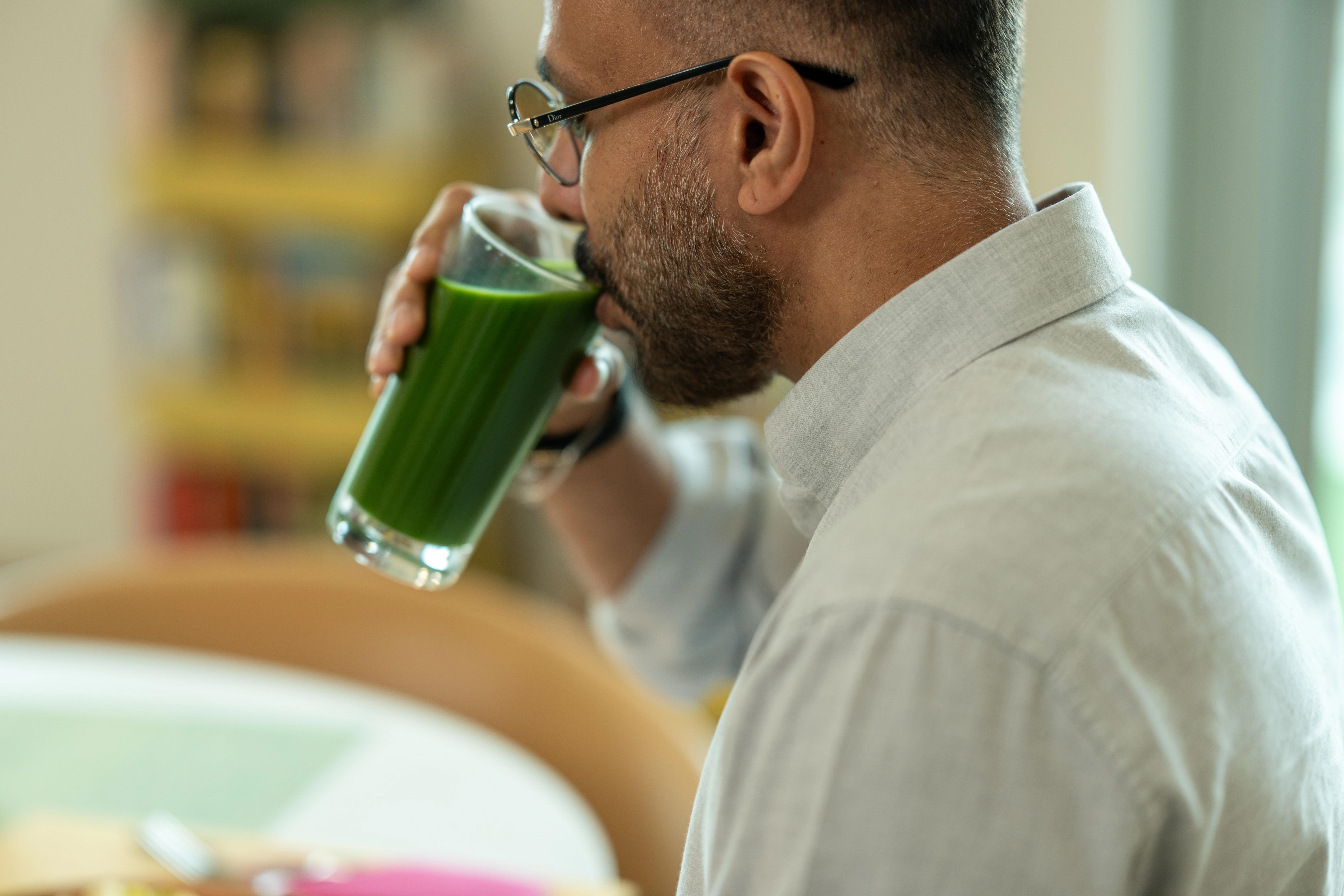 a man in glasses sips a green drink from a glass