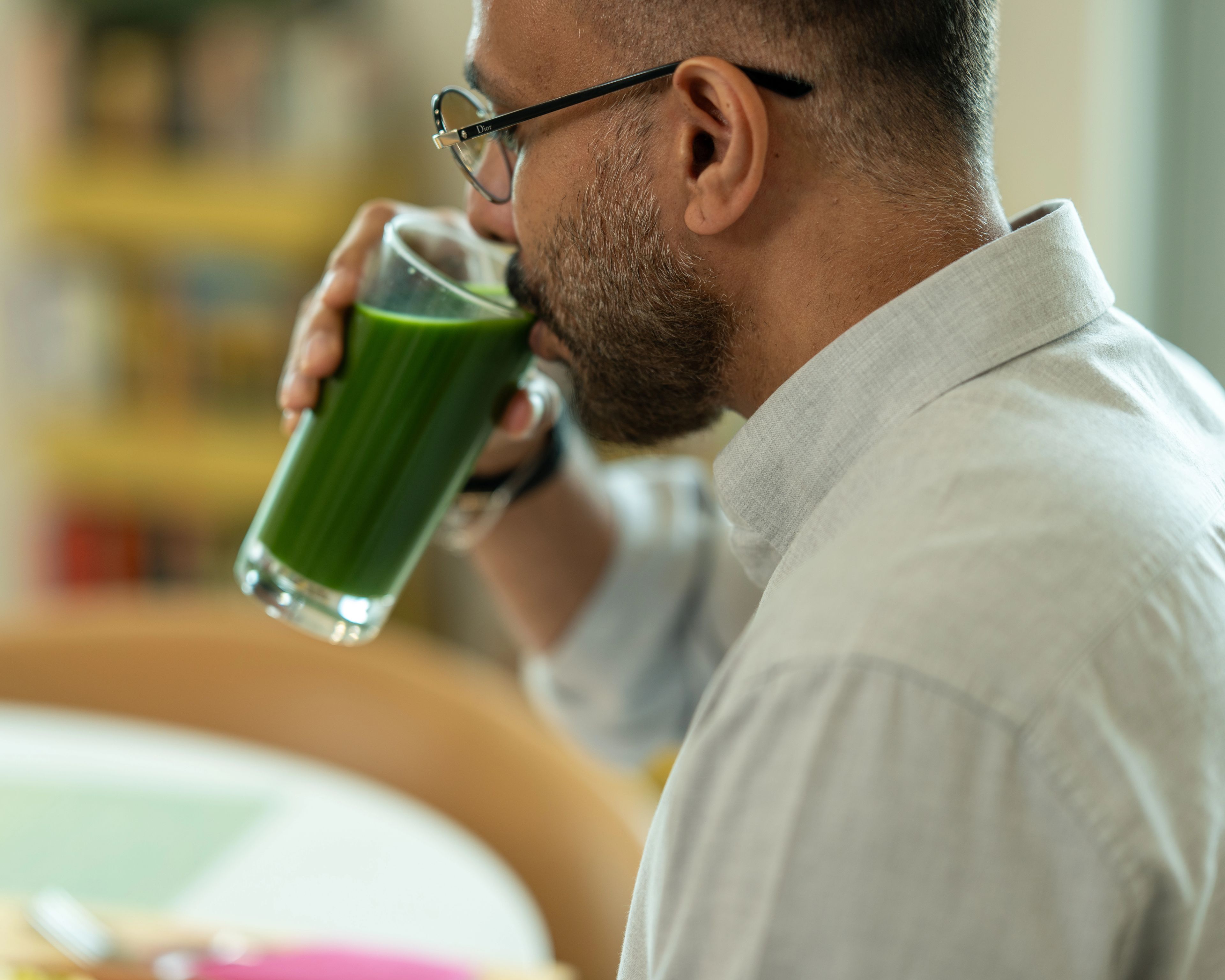 a man in glasses sips a green drink from a glass