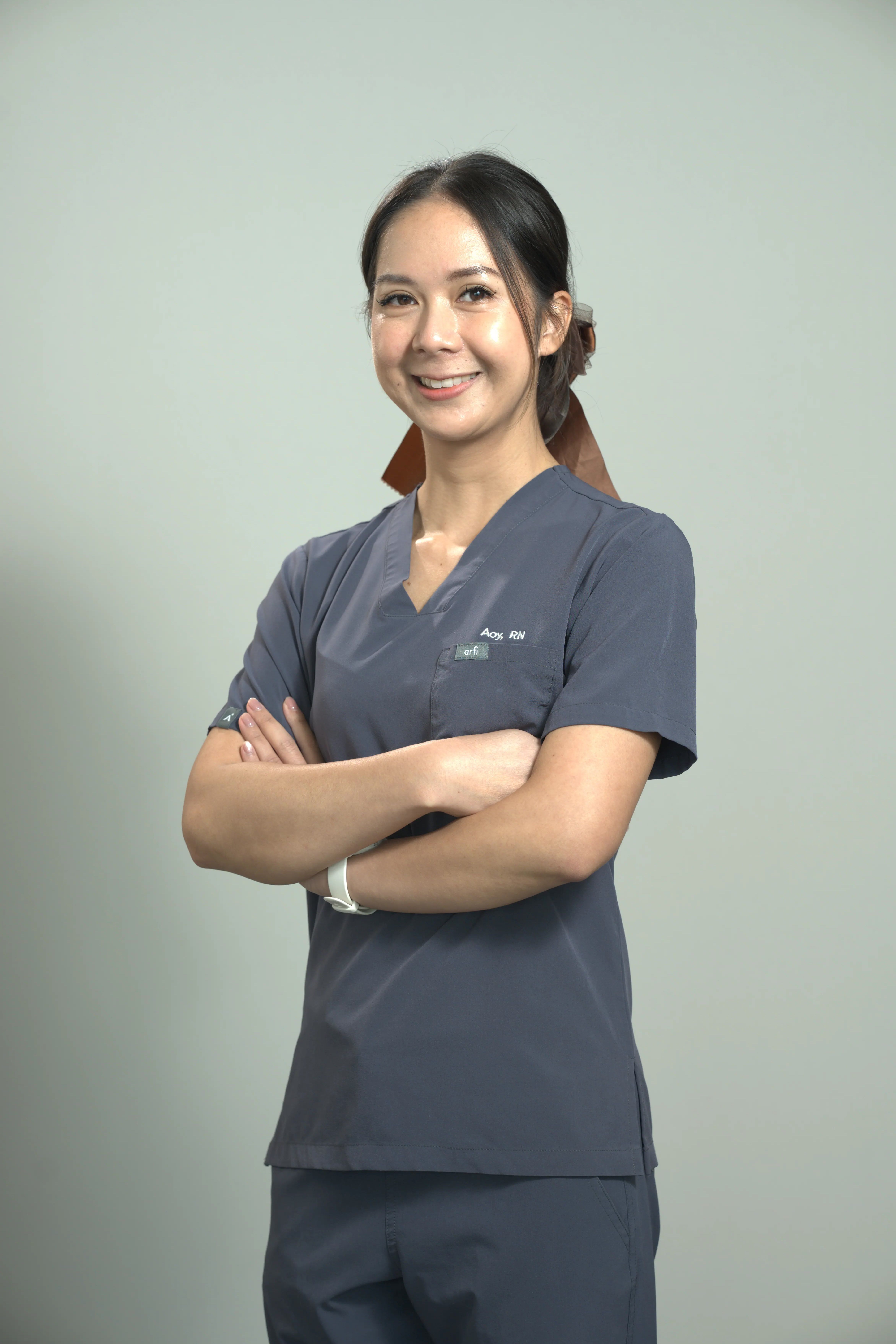Smiling lady with arms folded in grey nurse outfit