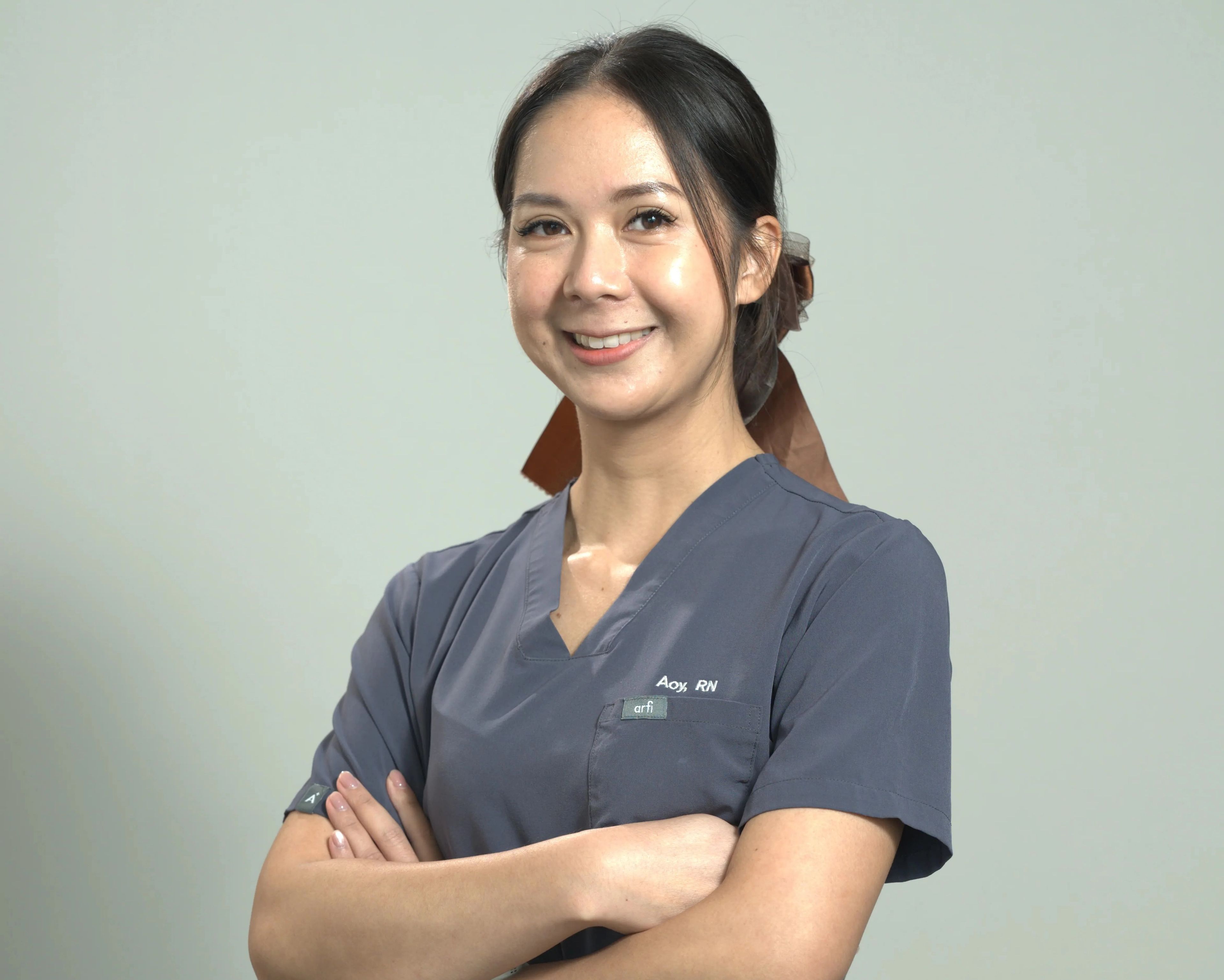 Smiling lady with arms folded in grey nurse outfit