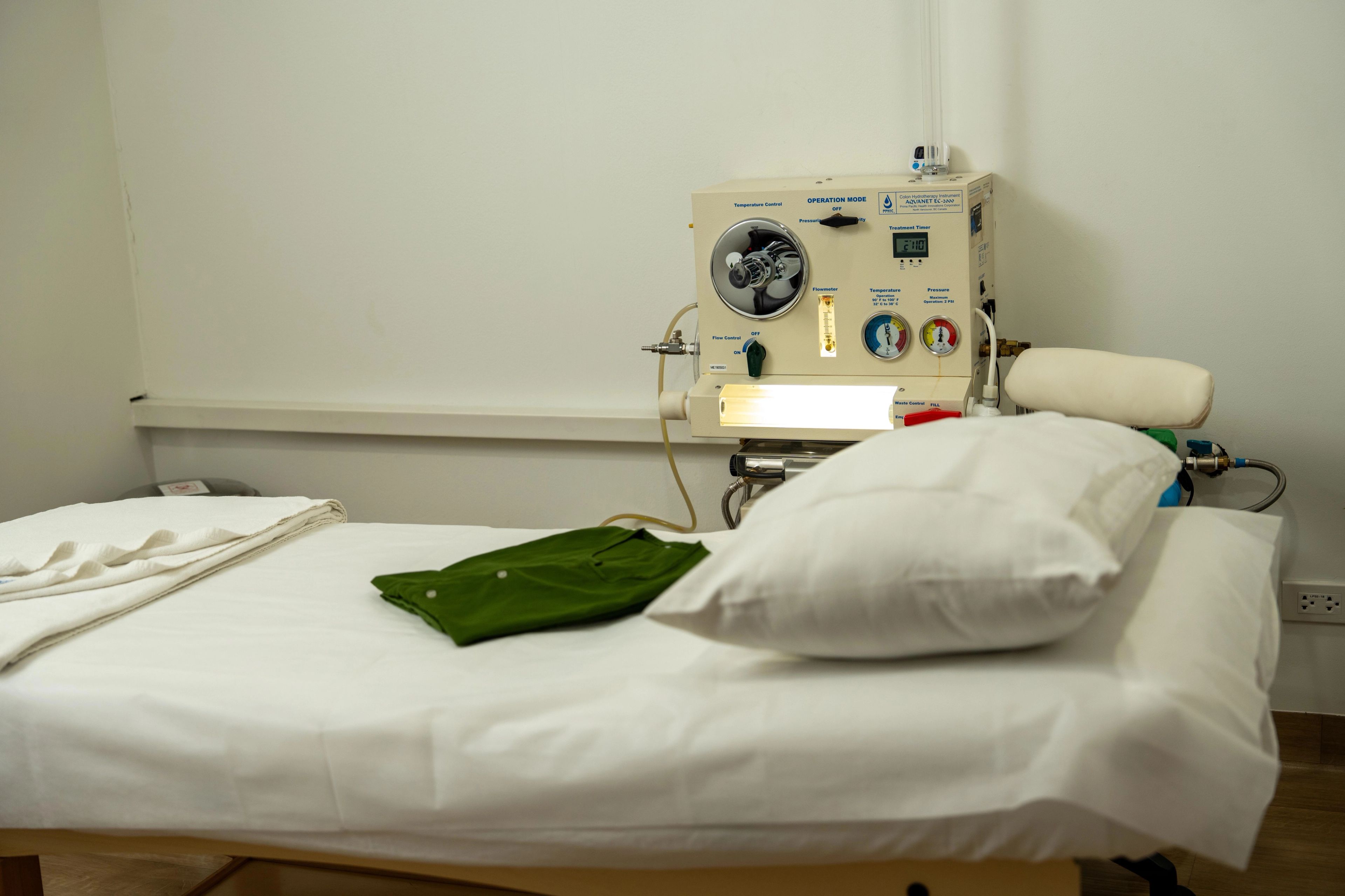 Hospital bed with pillow in front of a colonic therapy machine in a medical environment.