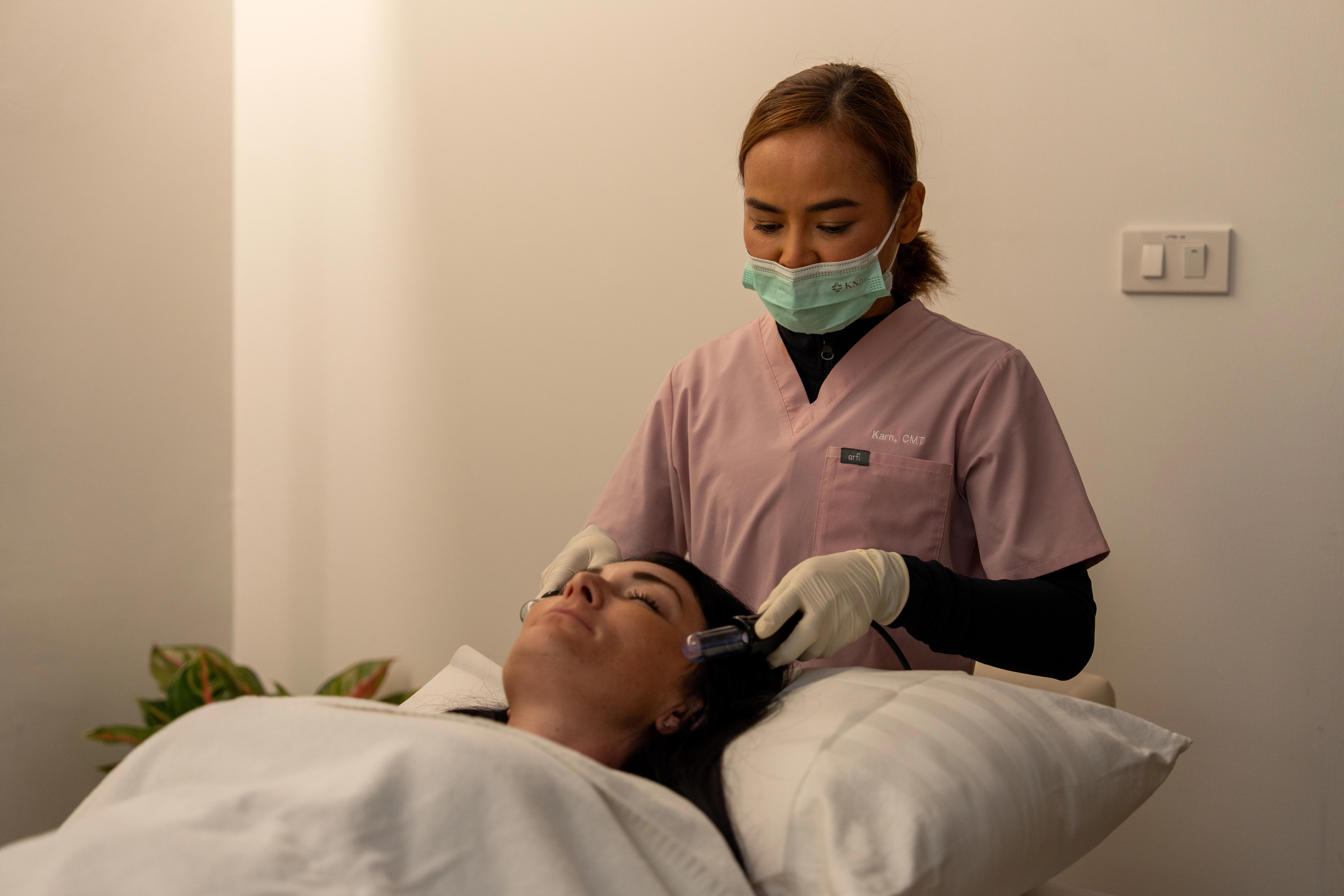 Female patient lays back on a pillow, while a medical professional wearing a mask, gloves, and scrubs performs lymphatic drainage.