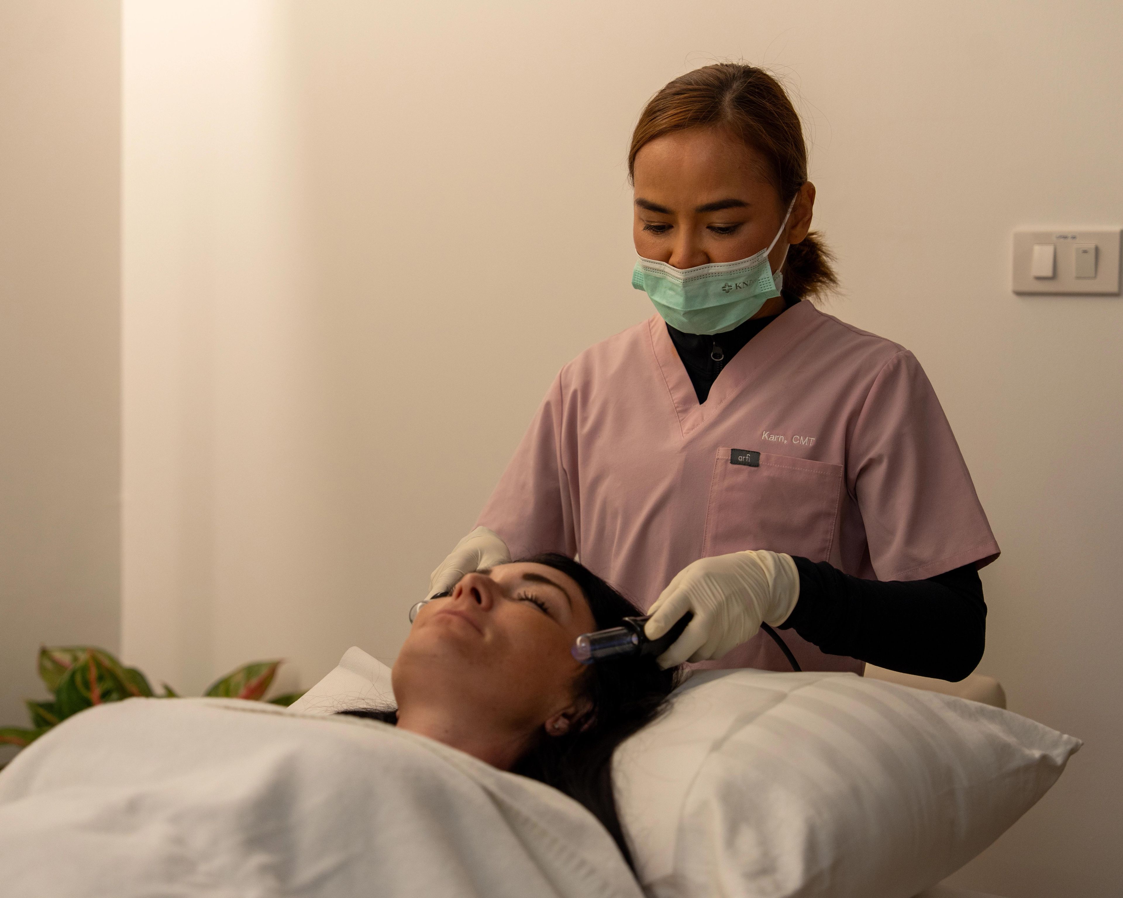 Female patient lays back on a pillow, while a medical professional wearing a mask, gloves, and scrubs performs lymphatic drainage.