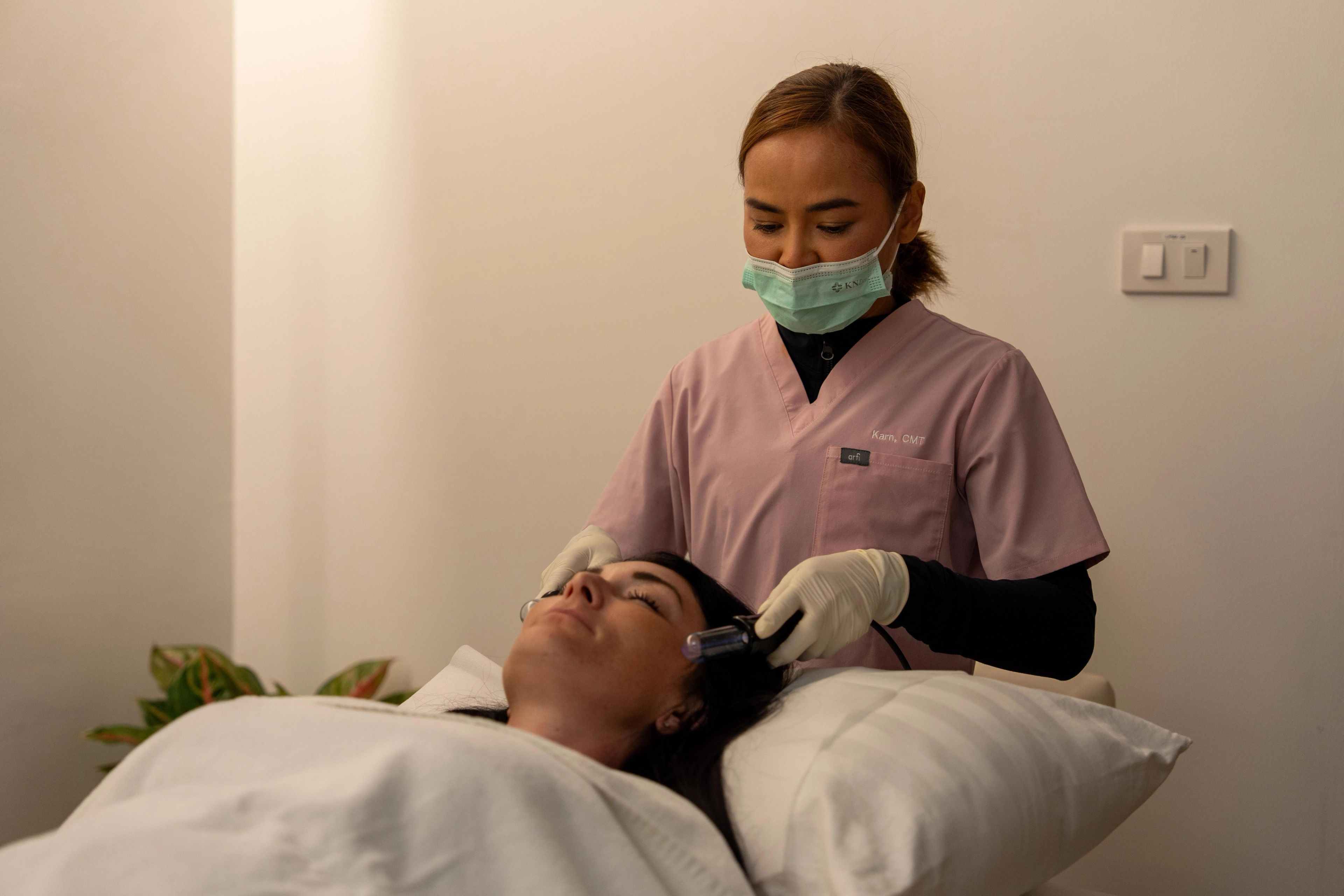 Female patient lays back on a pillow, while a medical professional wearing a mask, gloves, and scrubs performs lymphatic drainage.