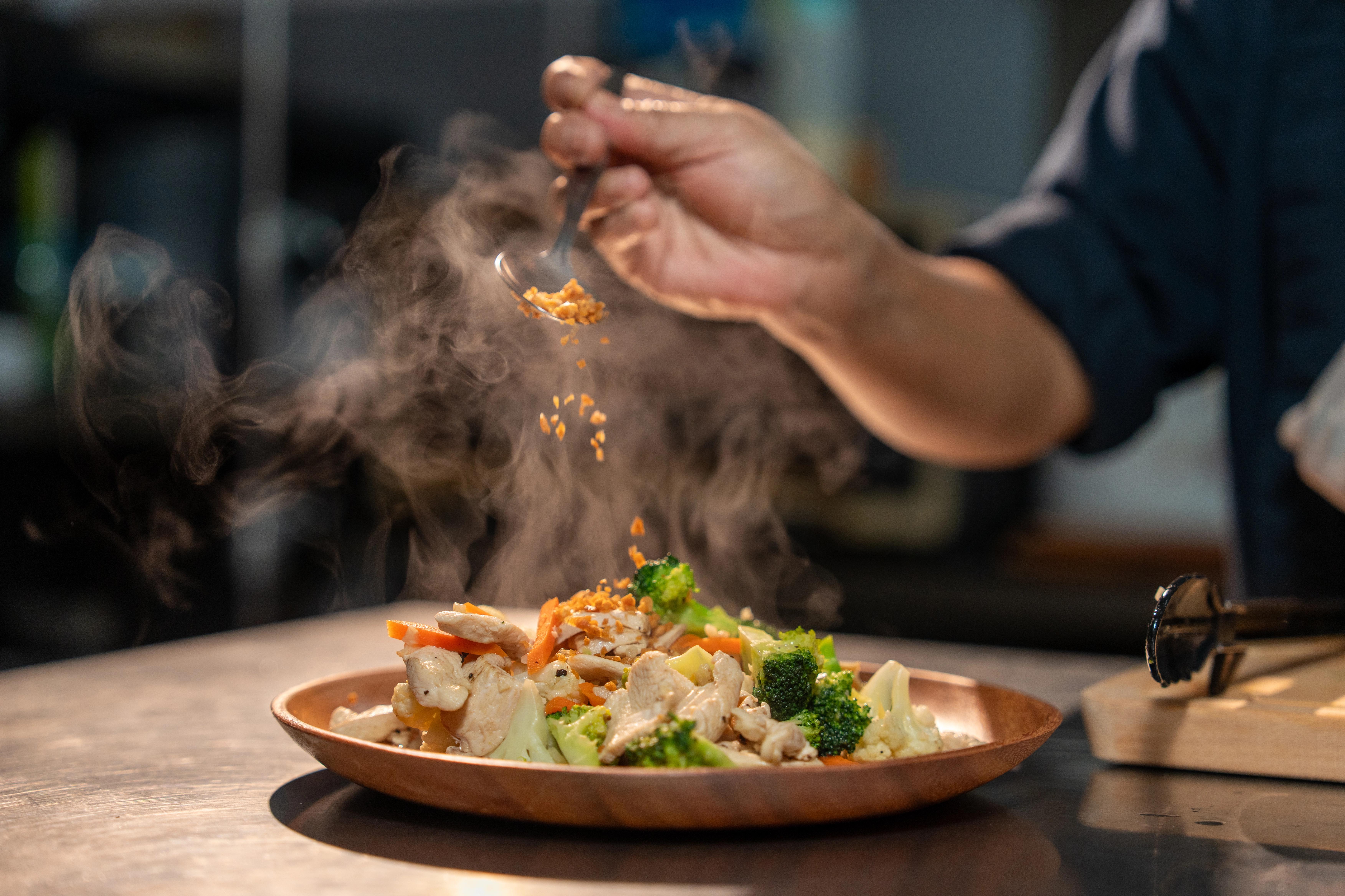 A close up of a plate of chicken and vegetables with steam rising from it.