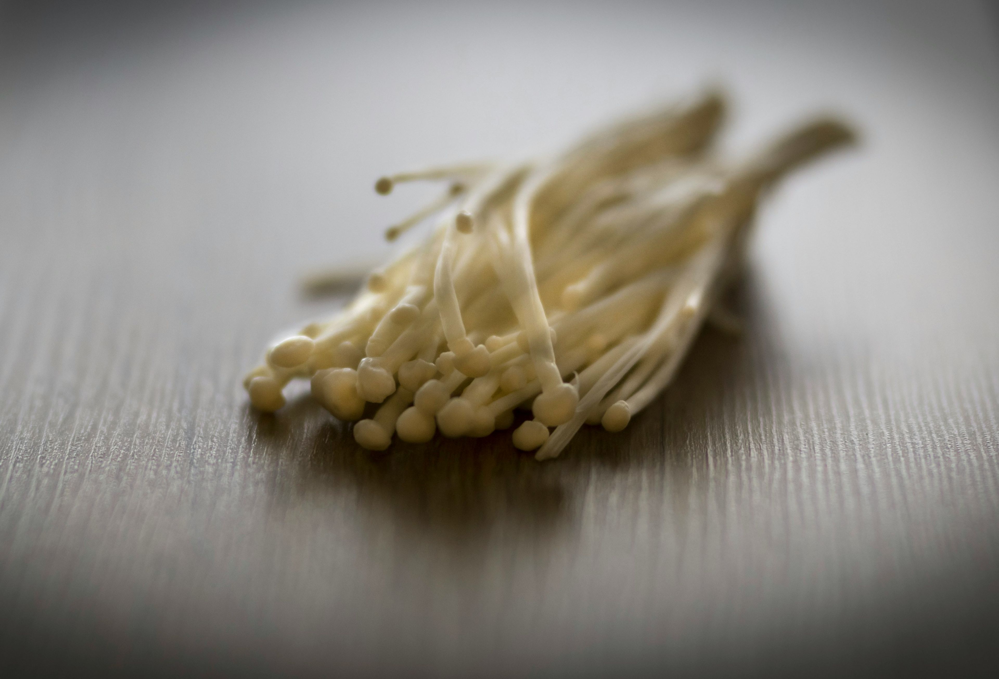 Fresh white enoki mushrooms with long, slender stems and small rounded caps, arranged together to highlight their distinctive appearance and nutritional qualities.