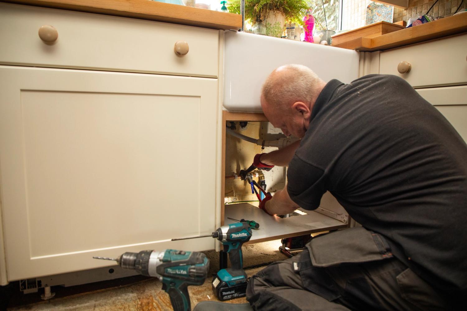 A plumber fixing a leak under a kitchen sink 
