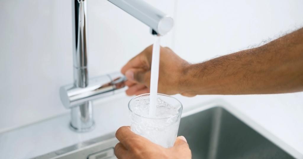 A person fills a glass of water using a tap in a sink
