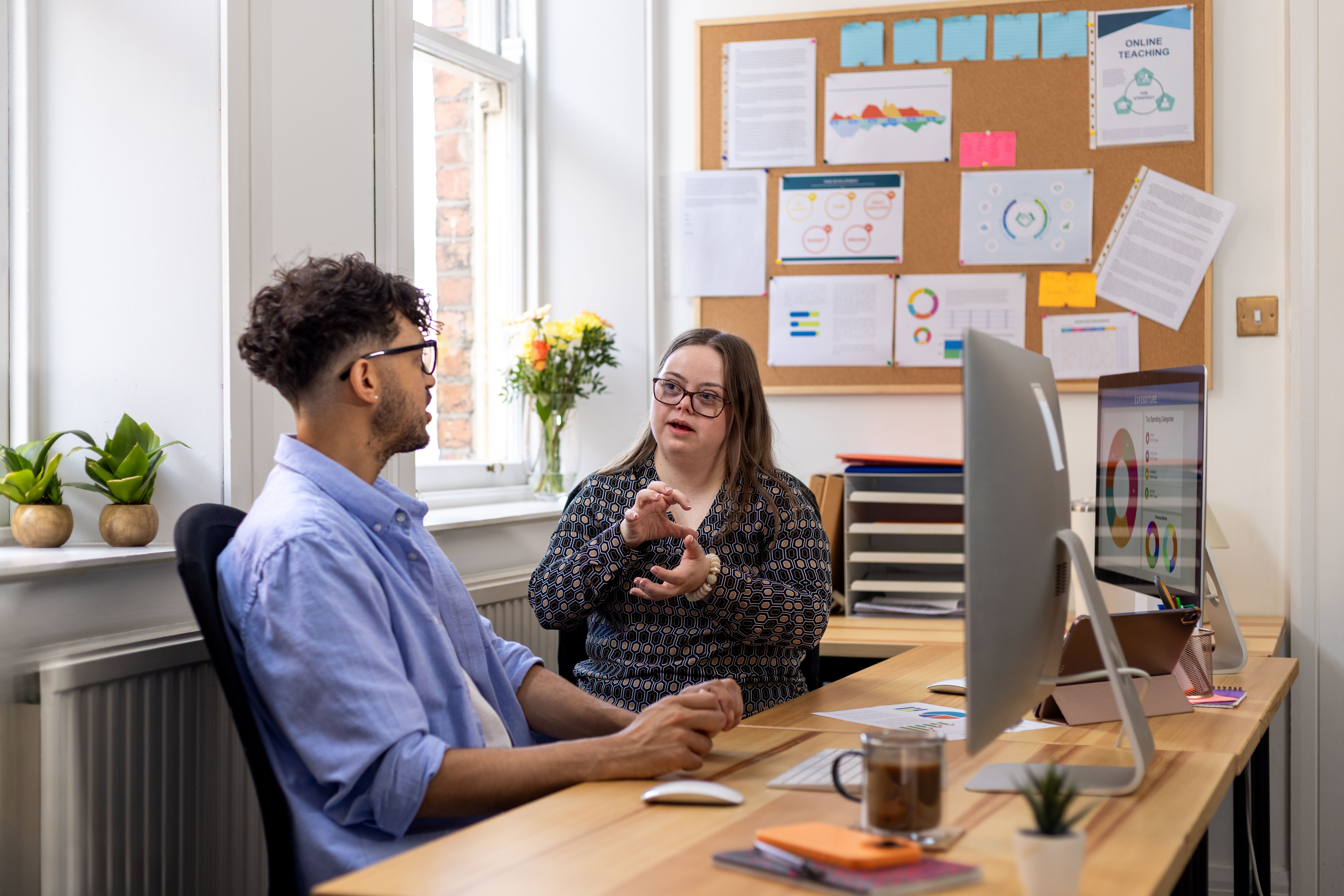 Two people chat around a computer in an office setting