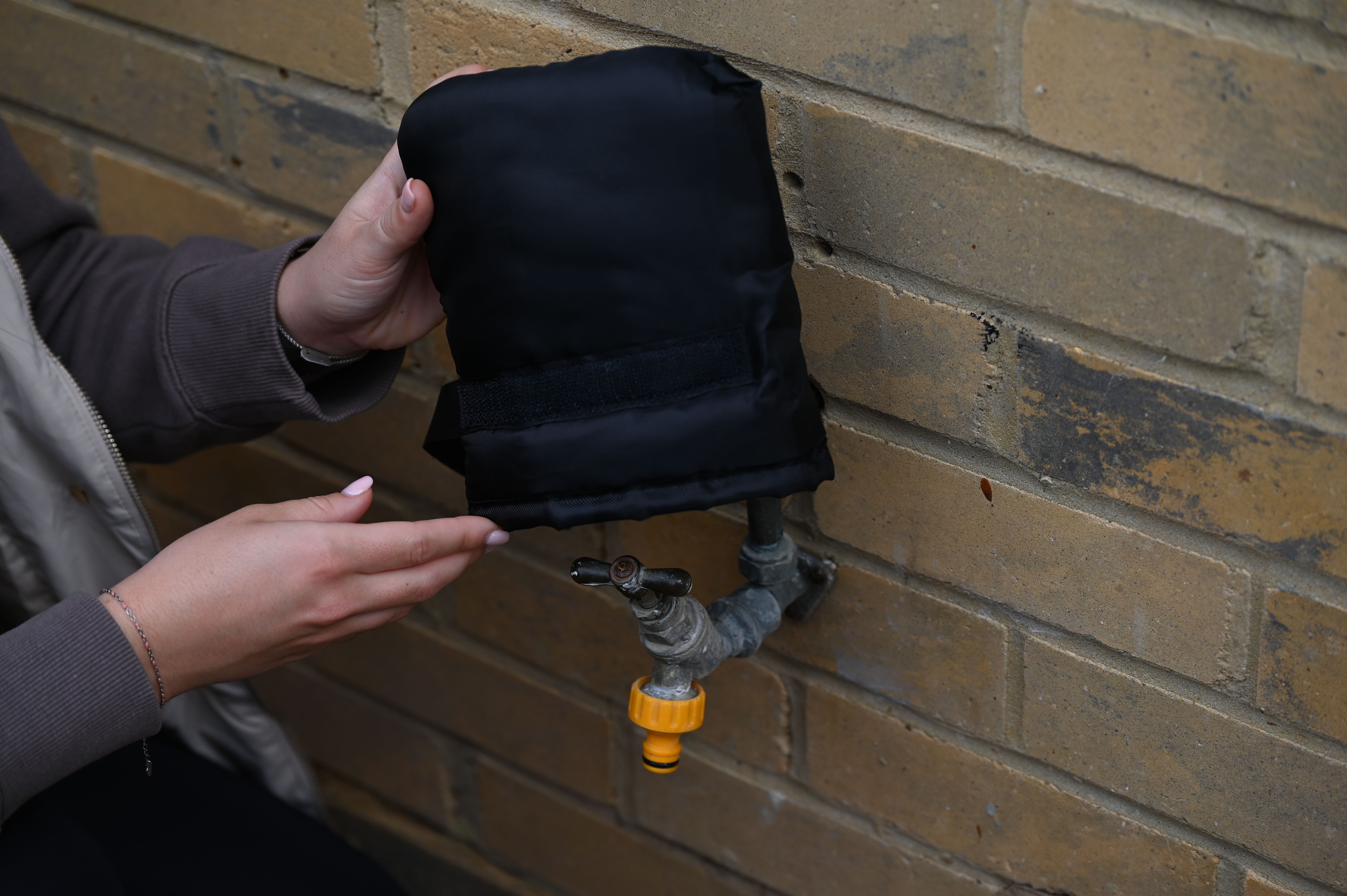 A person fits a tap jacket over an outdoor tap