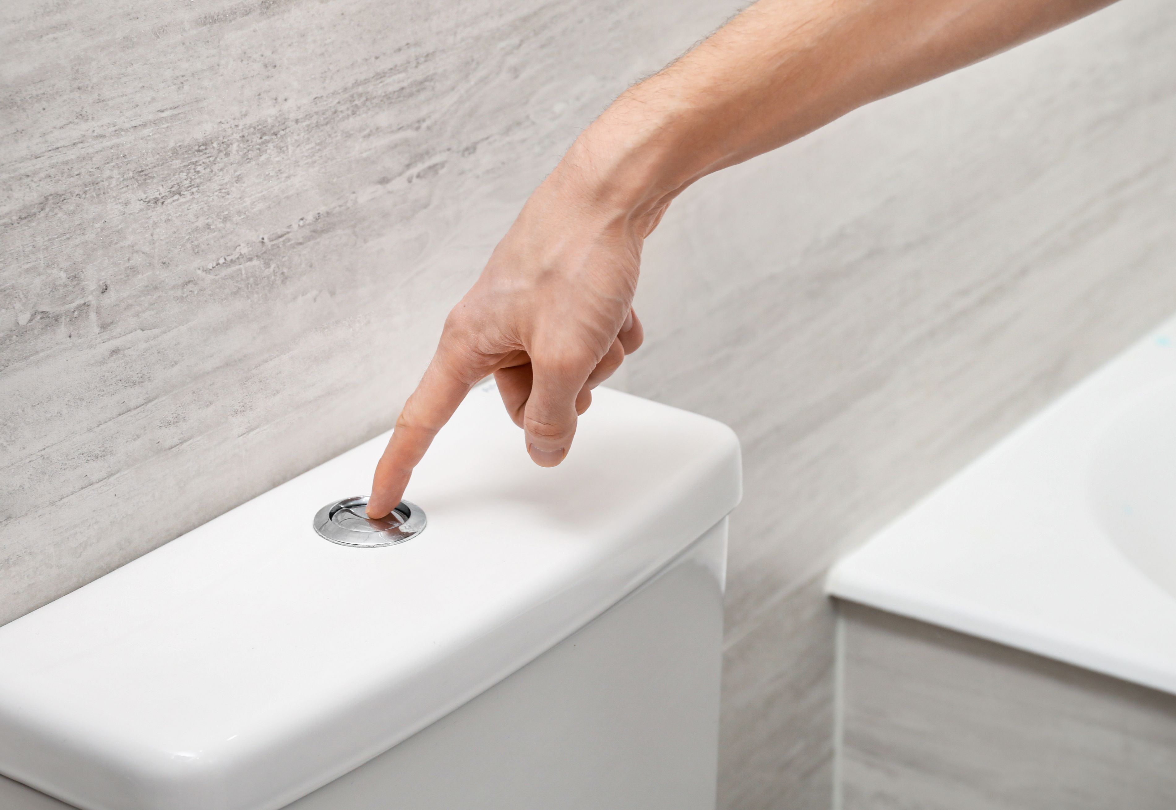 A person flushes a toilet using a dual-flush 