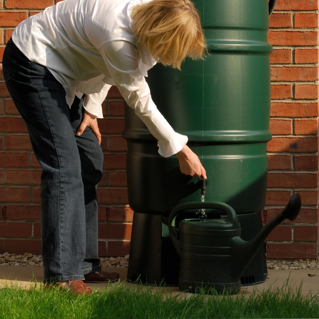 Photo of a person bending down collecting water from a water butt using a watering can