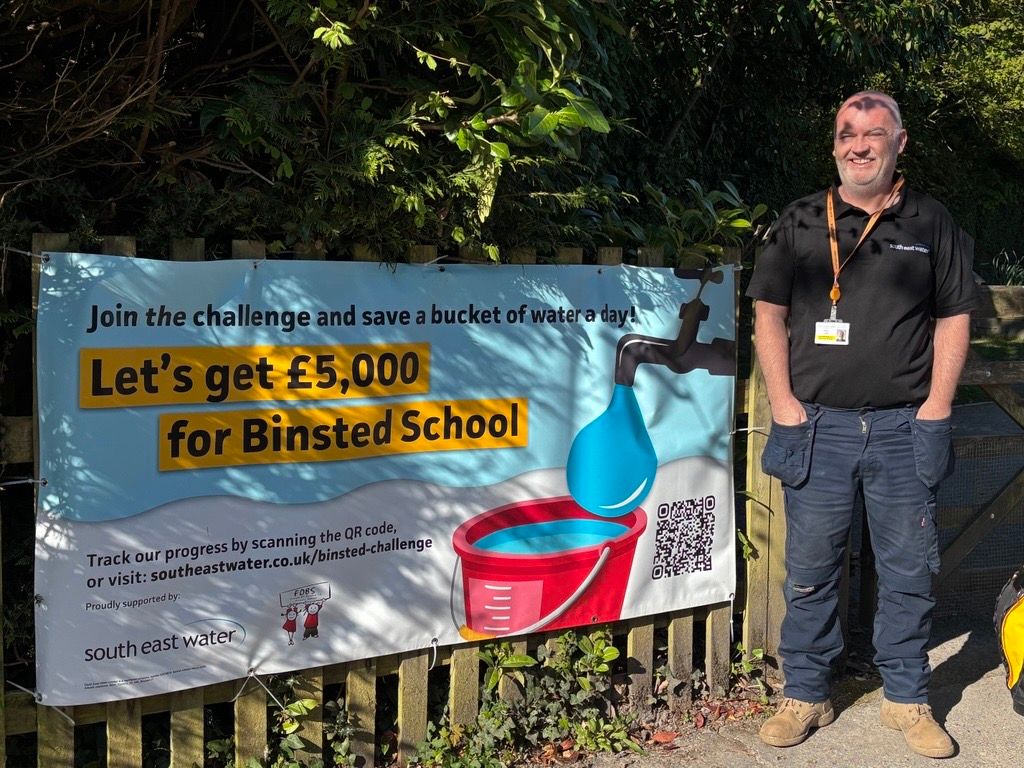 A South East Water staff member standing next to a water-saving challenge banner provided to Binsted School