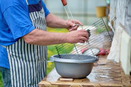 A man washes a bbq grill in a washing up bowl