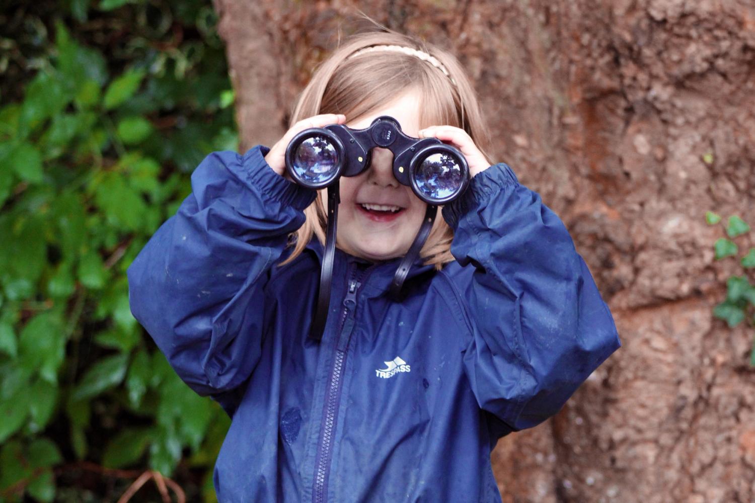 A school girl holds binoculars to her eyes
