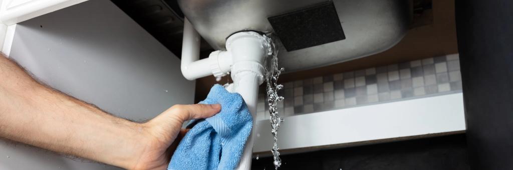 A person holds a cloth against a leaking pipe