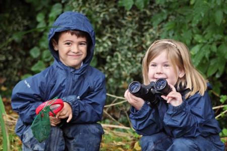 Two school children wearing rain jackets playing in a garden