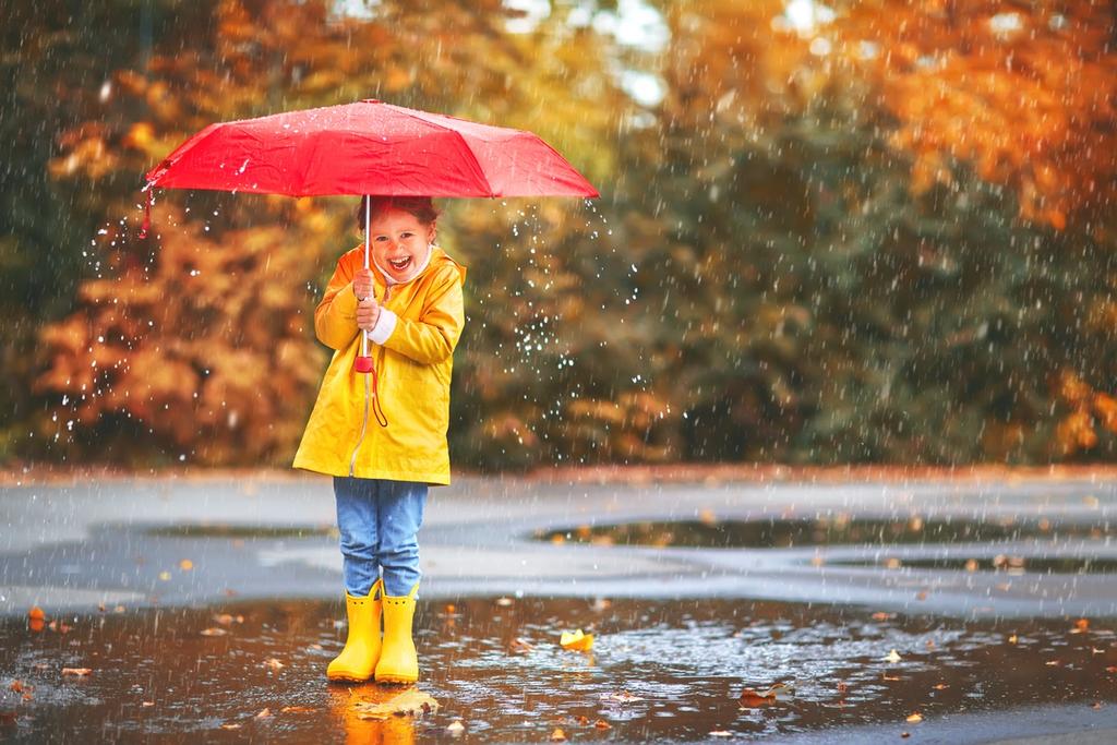 A girl in a yellow coat holds a red umbrella under the rain