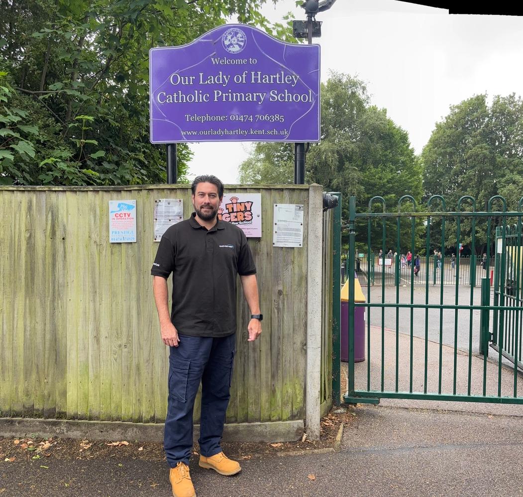 Our delivery partner stands next to the school sign for Our Lady of Hartley School