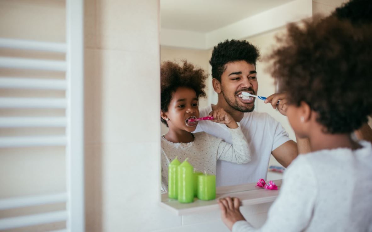 Photo of a man and a child brushing their teeth while looking in a mirror