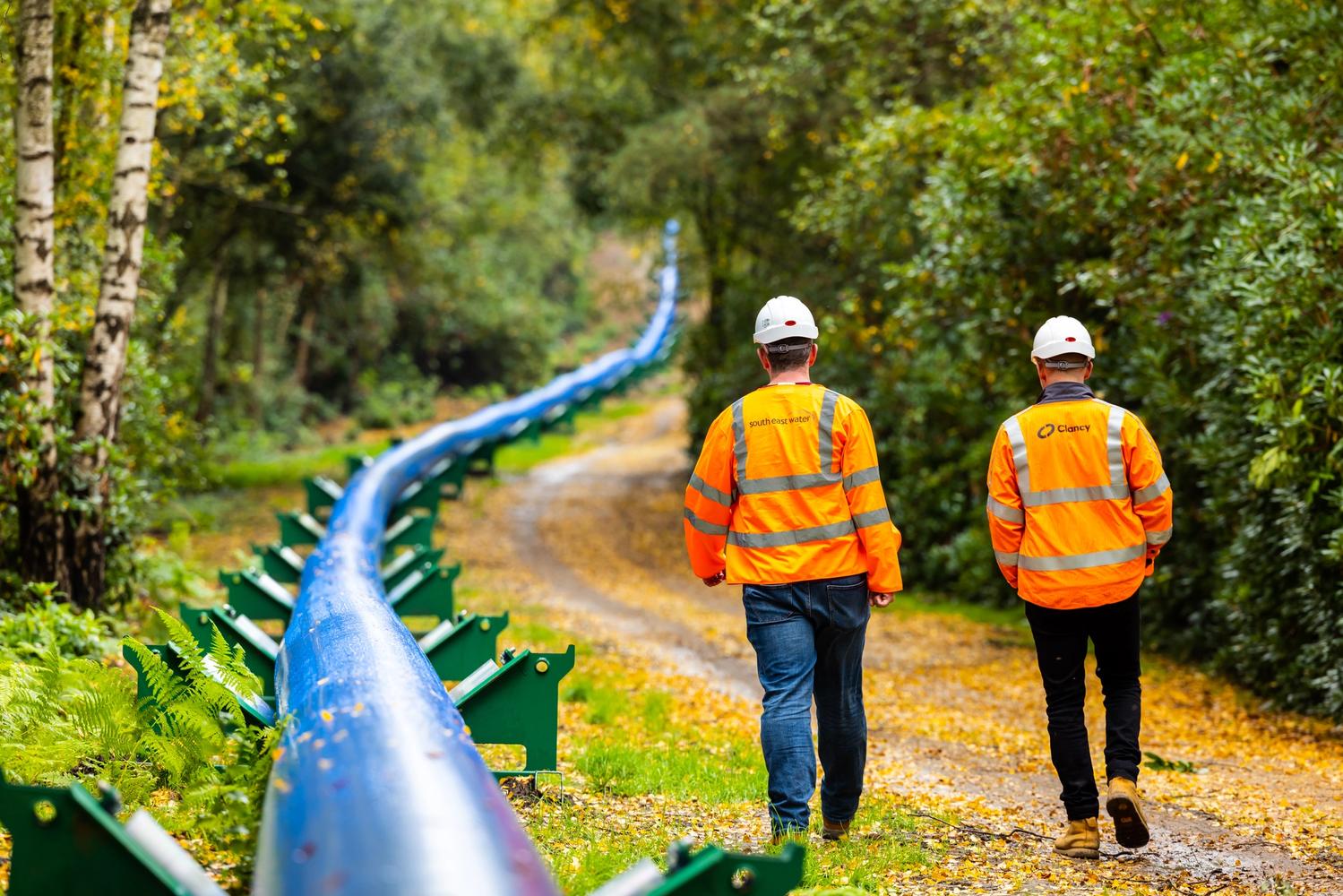 Two South East Water employees walking next to an unlaid pipe in a forest 