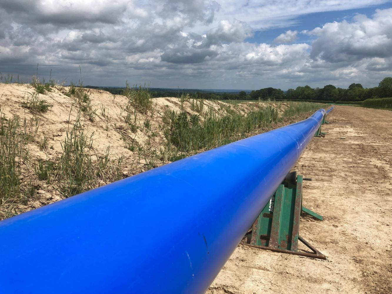 Image shows a blue stretch of pipe laid out across a field ready to be installed