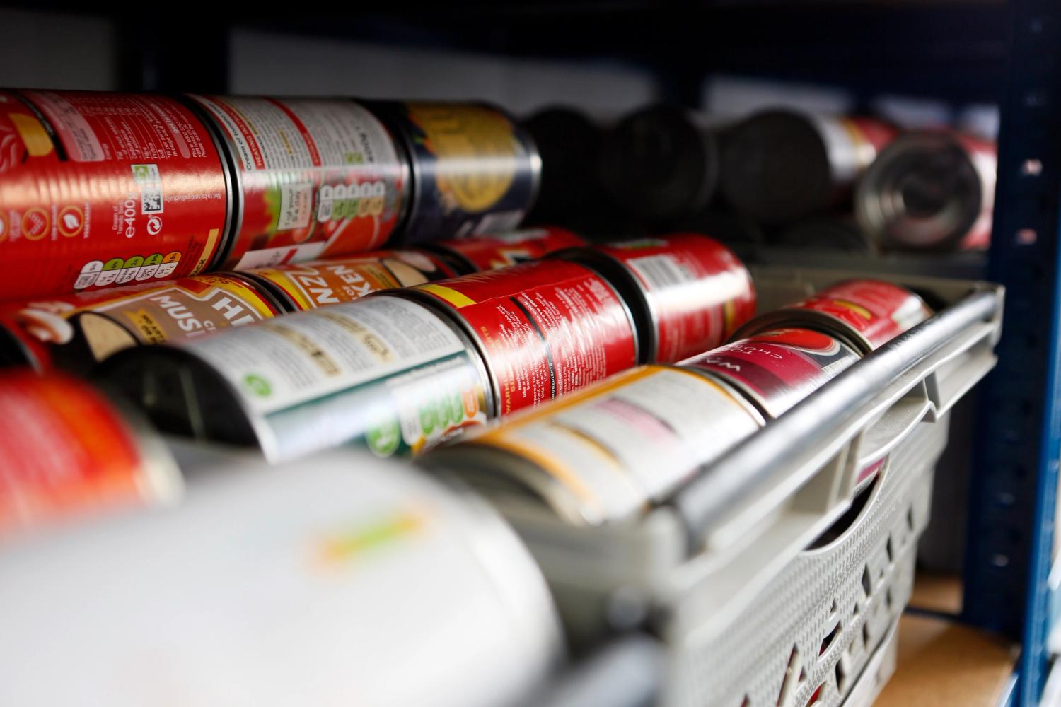 Cans stacked in large plastic trays on a shelf in a food bank