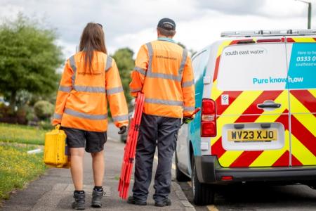 Two leakage technicians walking next to a South East Water van, carrying leakage equipment 