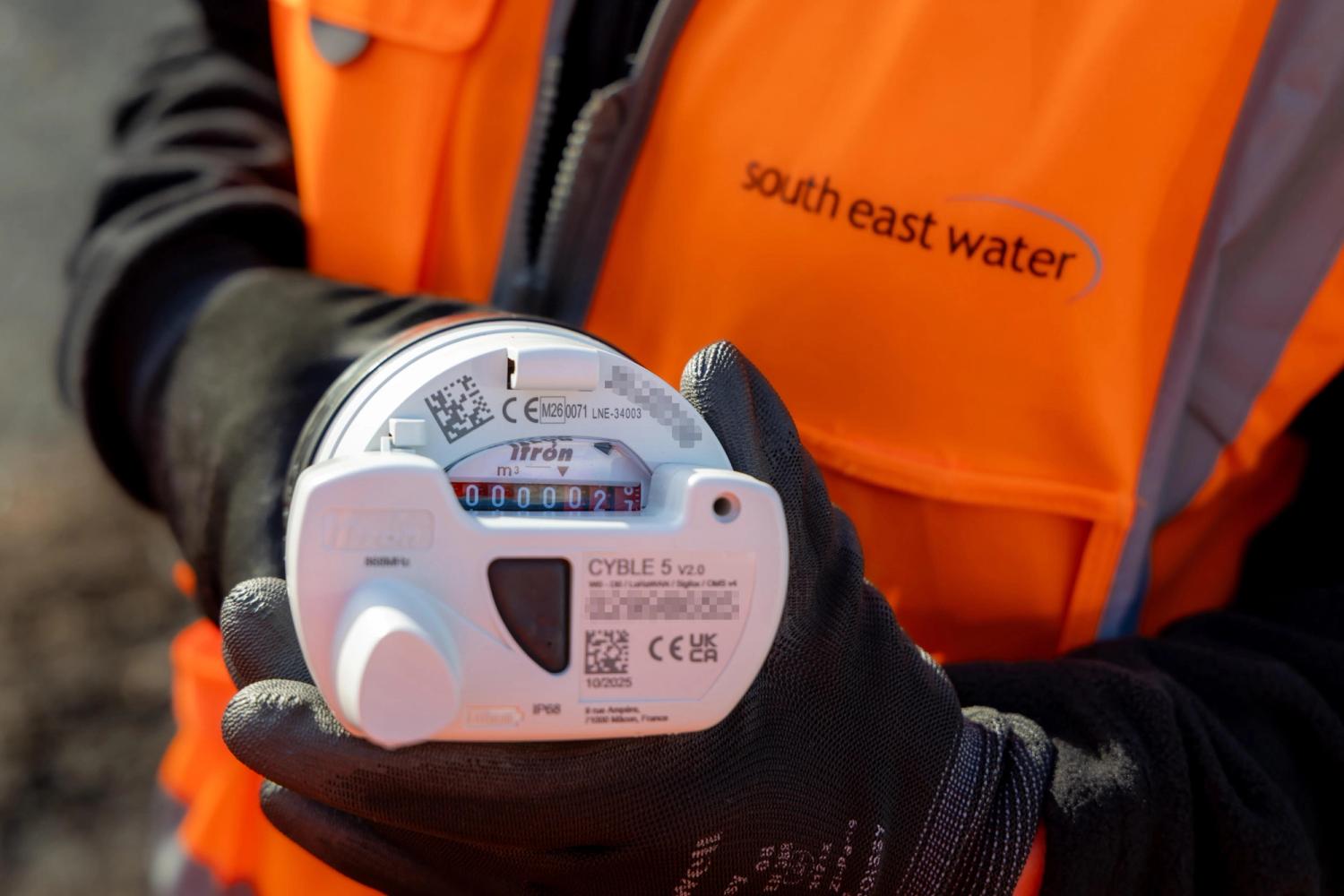 Close up of a smart water meter being held by a person wearing an orange high vis jacket and a black glove