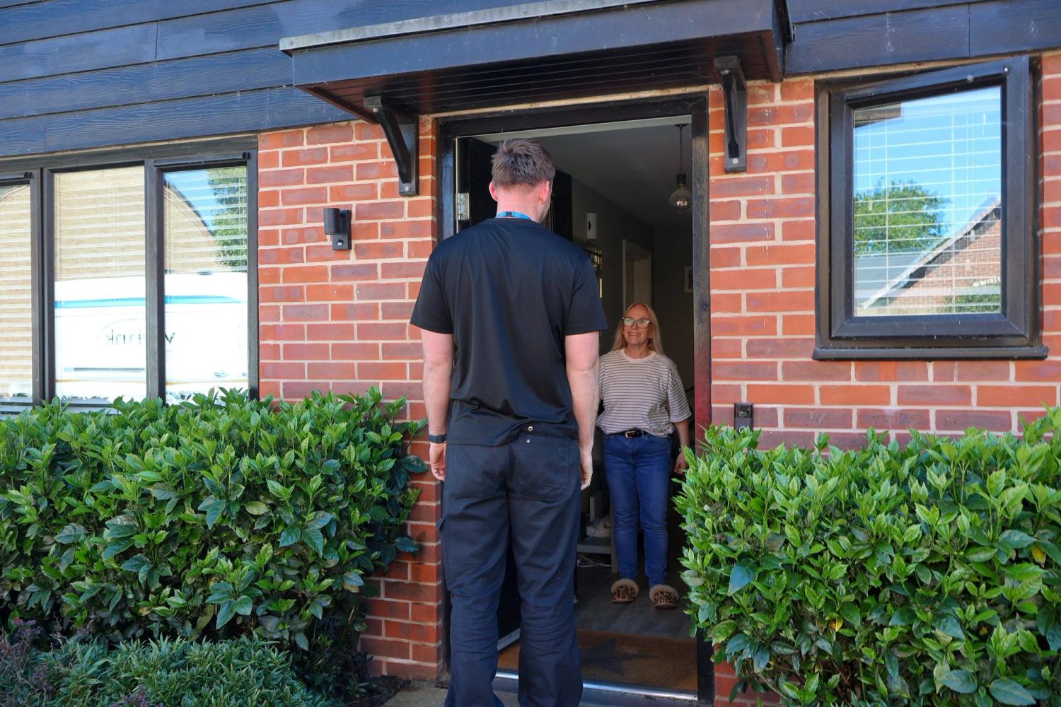 A Waterlink technician wearing a black branded t-shirt is stood chatting to a customer at her front door.
