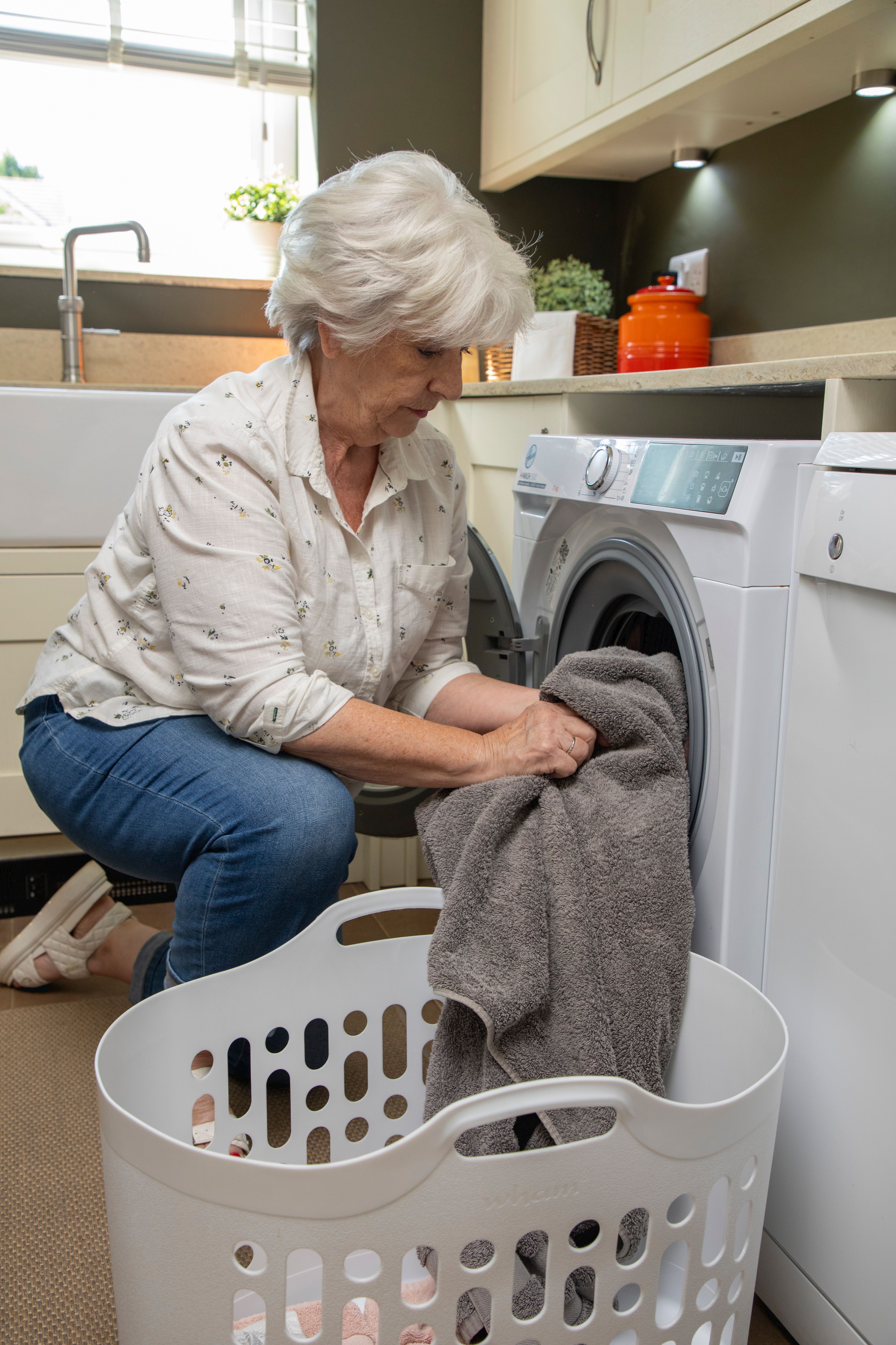 A woman kneeling down to put a grey towel in her washing machine.