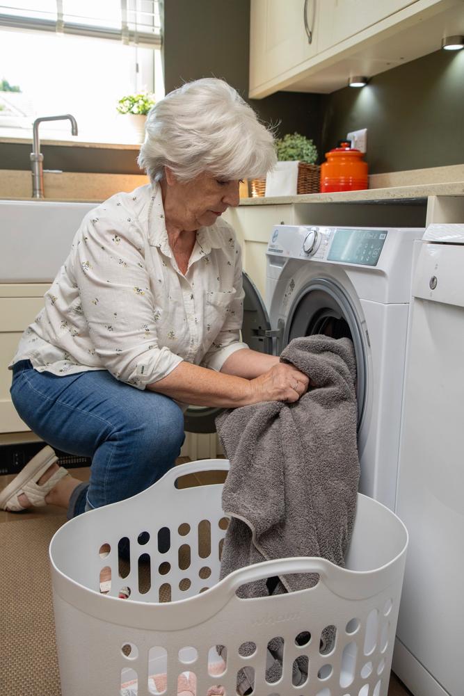 A woman kneeling down to put a grey towel in her washing machine.