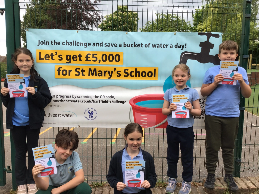 Pupils of St Mary's School holding a challenge leaflet and stood in front of the challenge banner attached to the school fence.