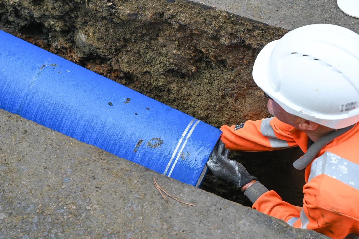 An engineer wearing a protective hat and orange uniform places pipe into the ground.