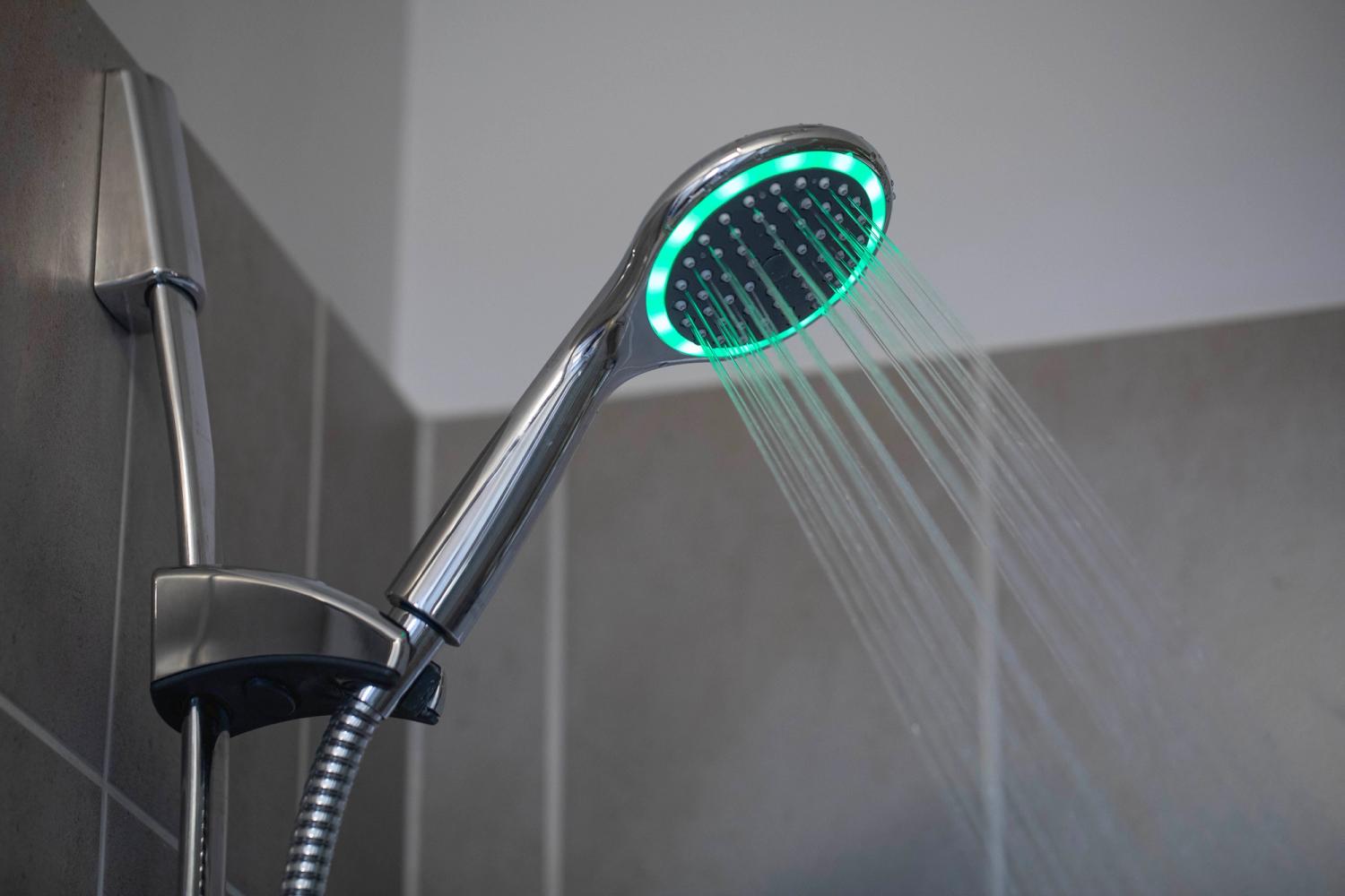 A metal shower with a colour-changing shower head fitted. It is glowing green.