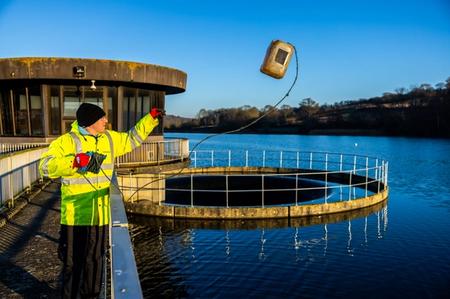 An Environmental Catchment Scientist dressed in hi-vis throwing a large container into our surface water reservoir at Ardingly.