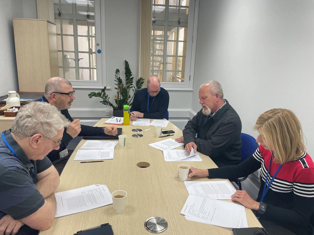 Photo of 5 South East Water employees sat around a table discussing a report that they are all reading