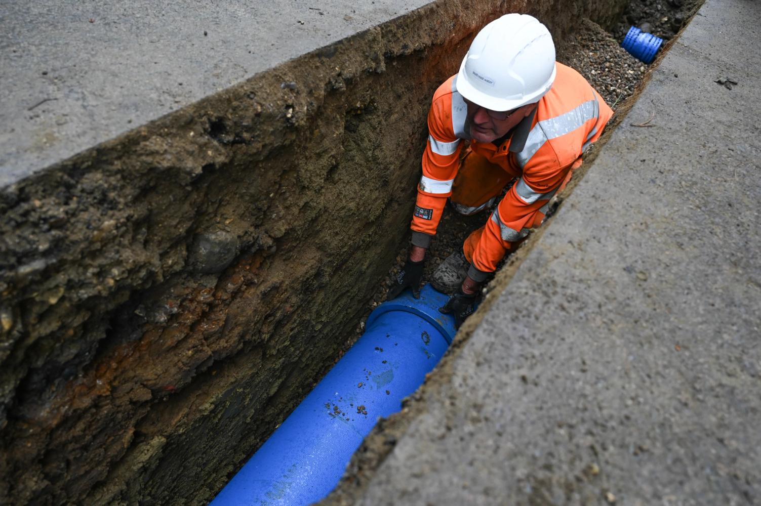A technician, wearing orange high visibility clothing and a hard hat, installing a pipe.