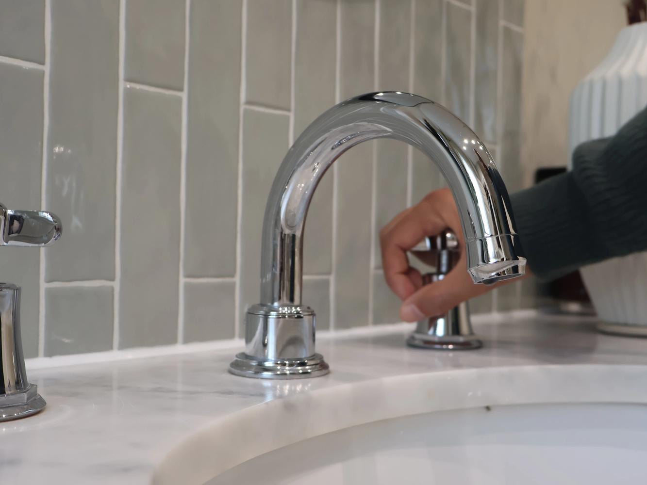 An image of a sink within a stone worktop. A person has their hand on the cold tap. There is no running water.