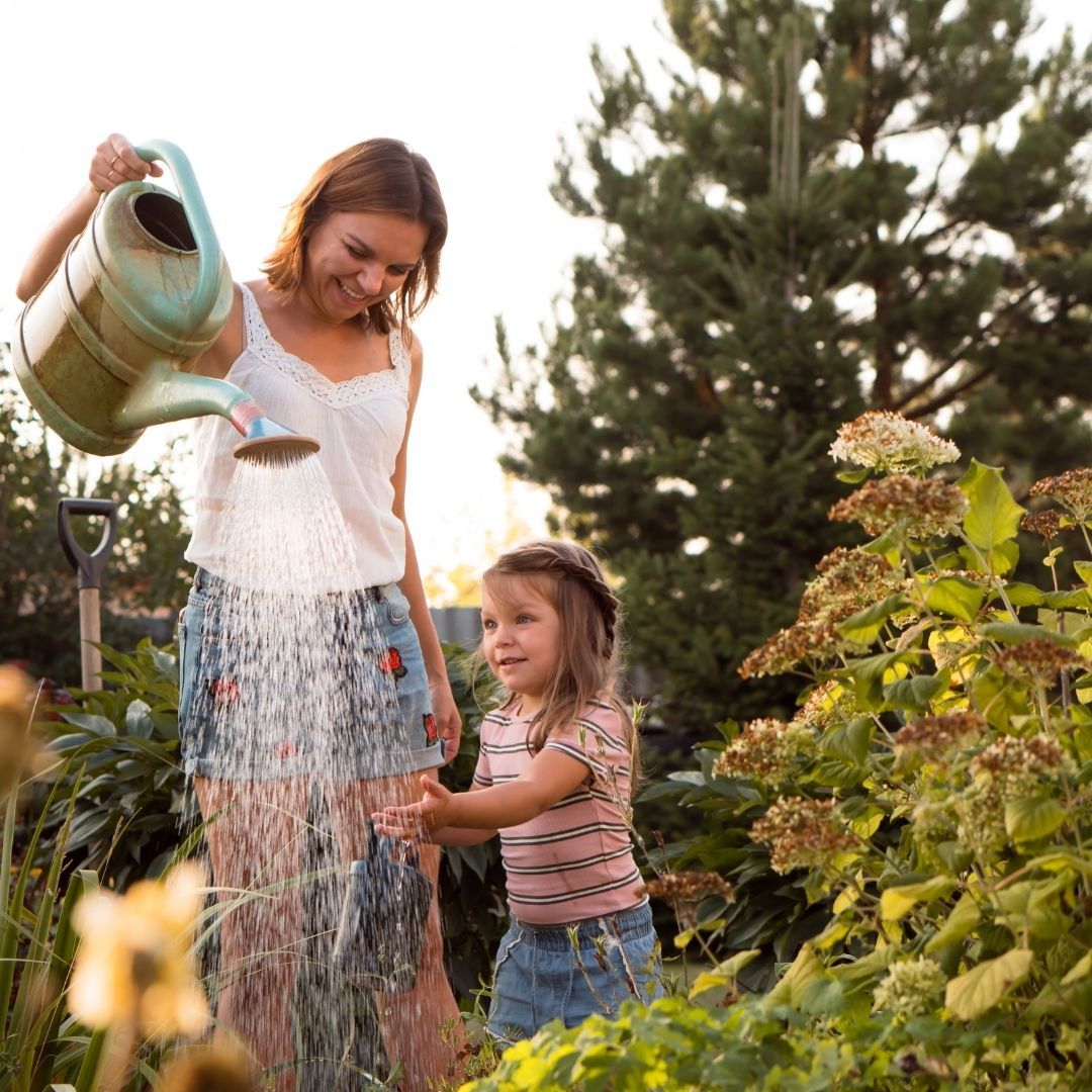A woman holding a watering can with a child nearby