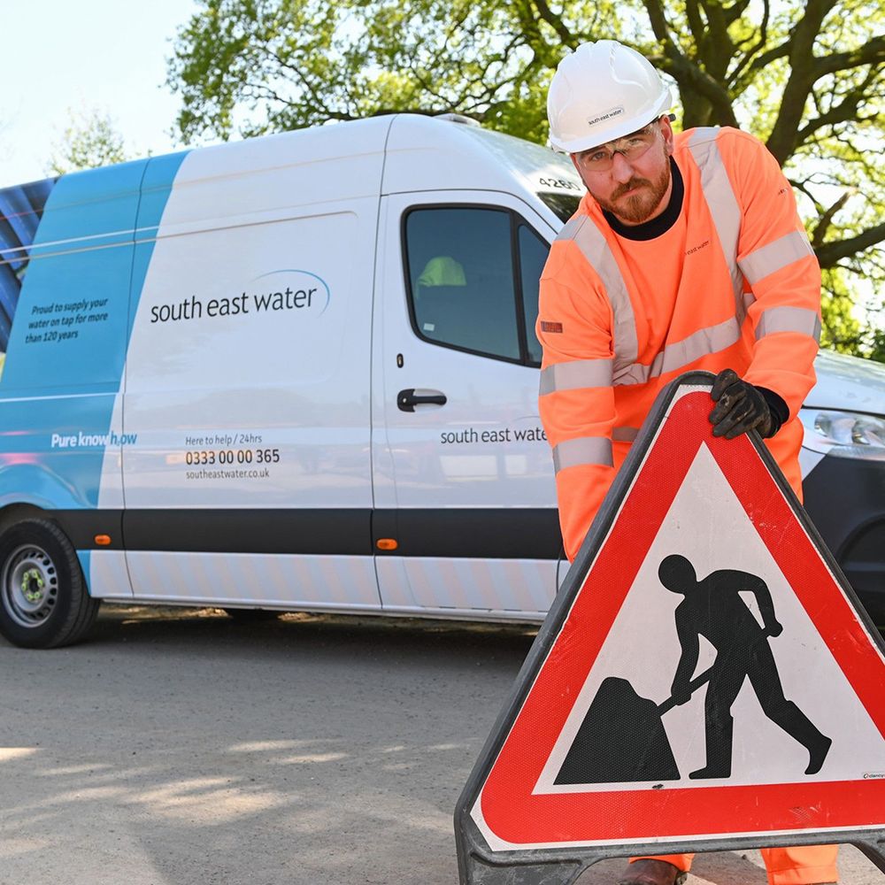 A man in high-visibility clothing puts out a roadworks sign in front of a South East Water van