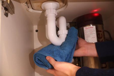 A warm towel is being used to thaw a frozen pipe under the kitchen sink.