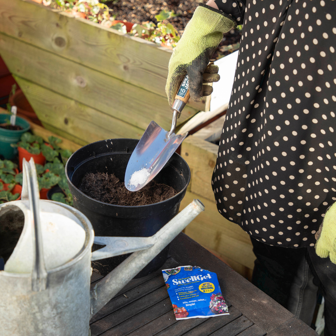 A woman is adding SwellGel crystals to the soil in her plant pot.