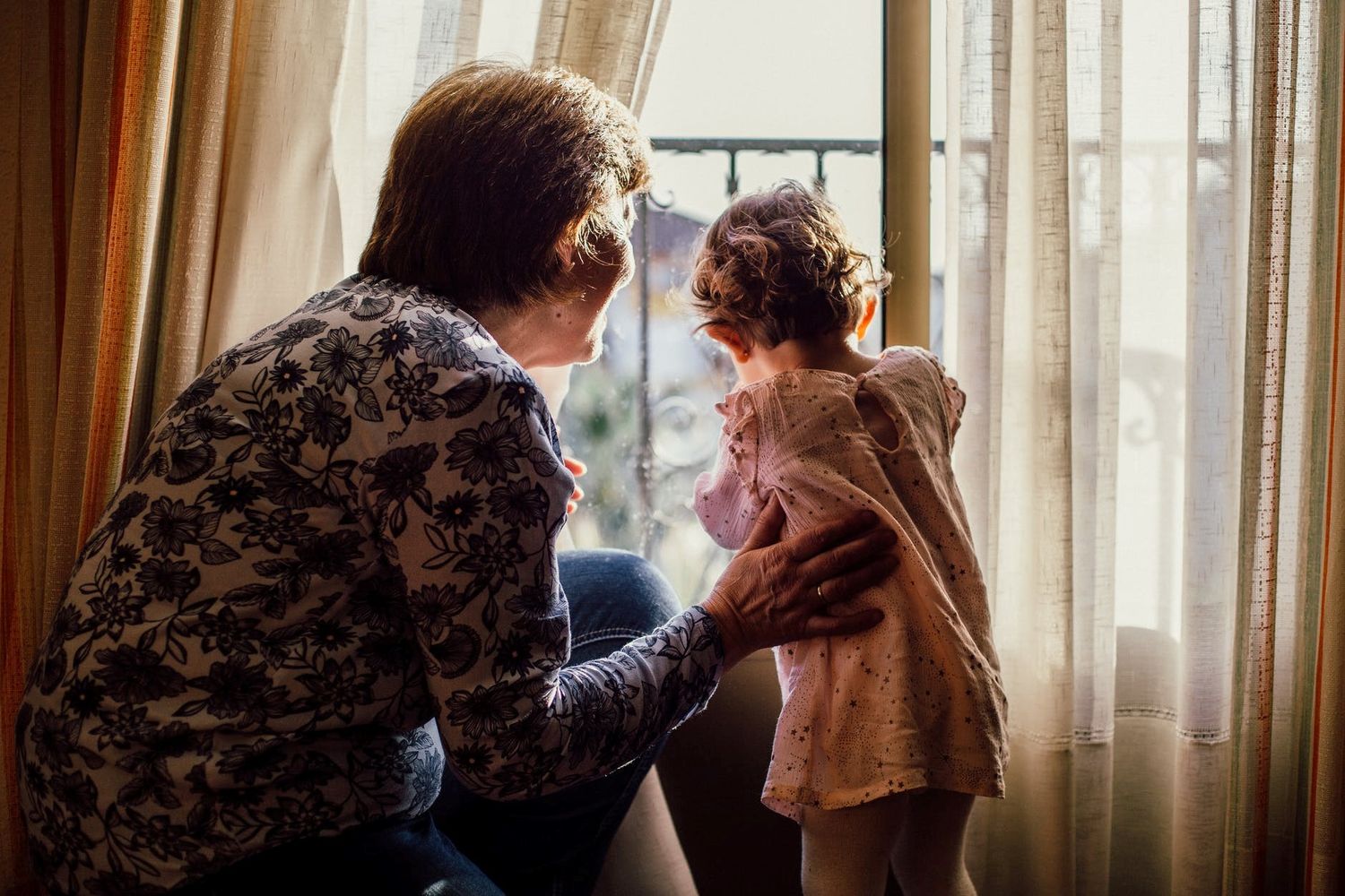 Elderly lady and young girl in a pink dress looking out of the window. 