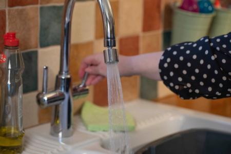 A person turning on a kitchen tap where a water-saving ap aerator has been fitted.