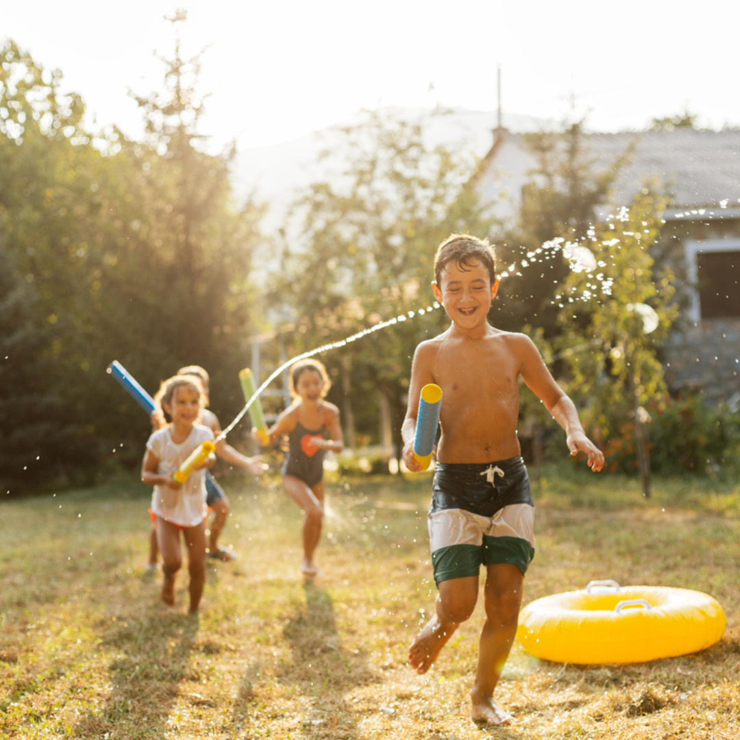 Four children are playing in a garden with water blasters.