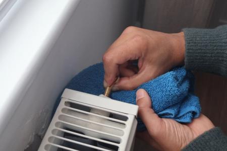A man has inserted a radiator key into the radiator to bleed it.