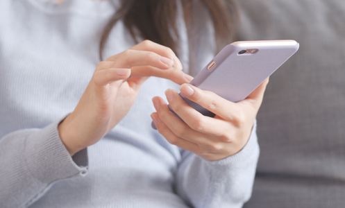 Woman wearing a grey jumper holding a phone with both hands.