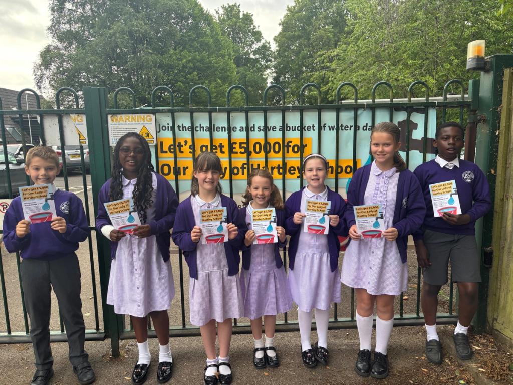Pupils of Our Lady of Hartley School holding a challenge leaflet and stood in front of the challenge banner attached to the school fence.