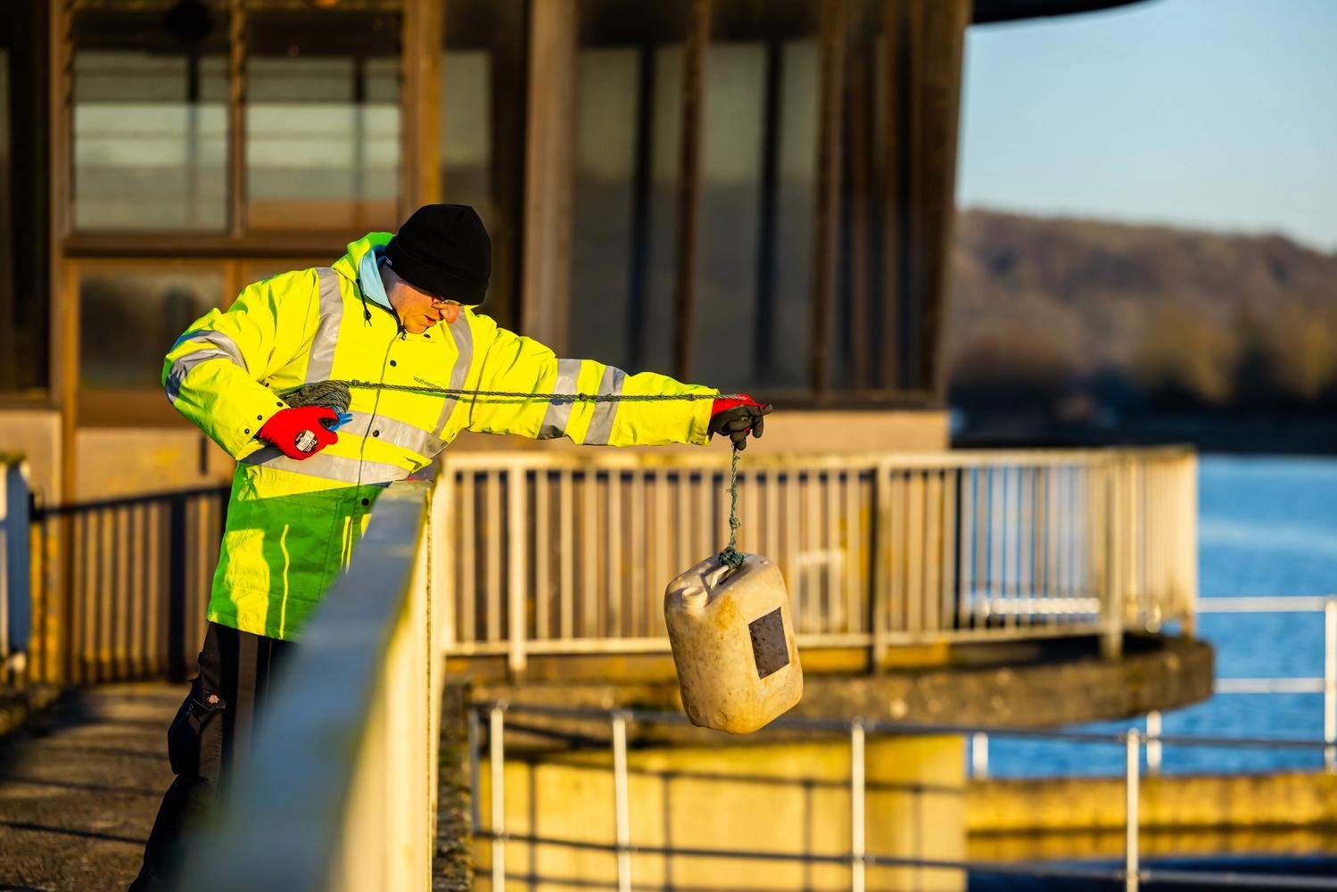 South East Water employee using a rod and rope to lower a container into the reservoir water to collect a sample